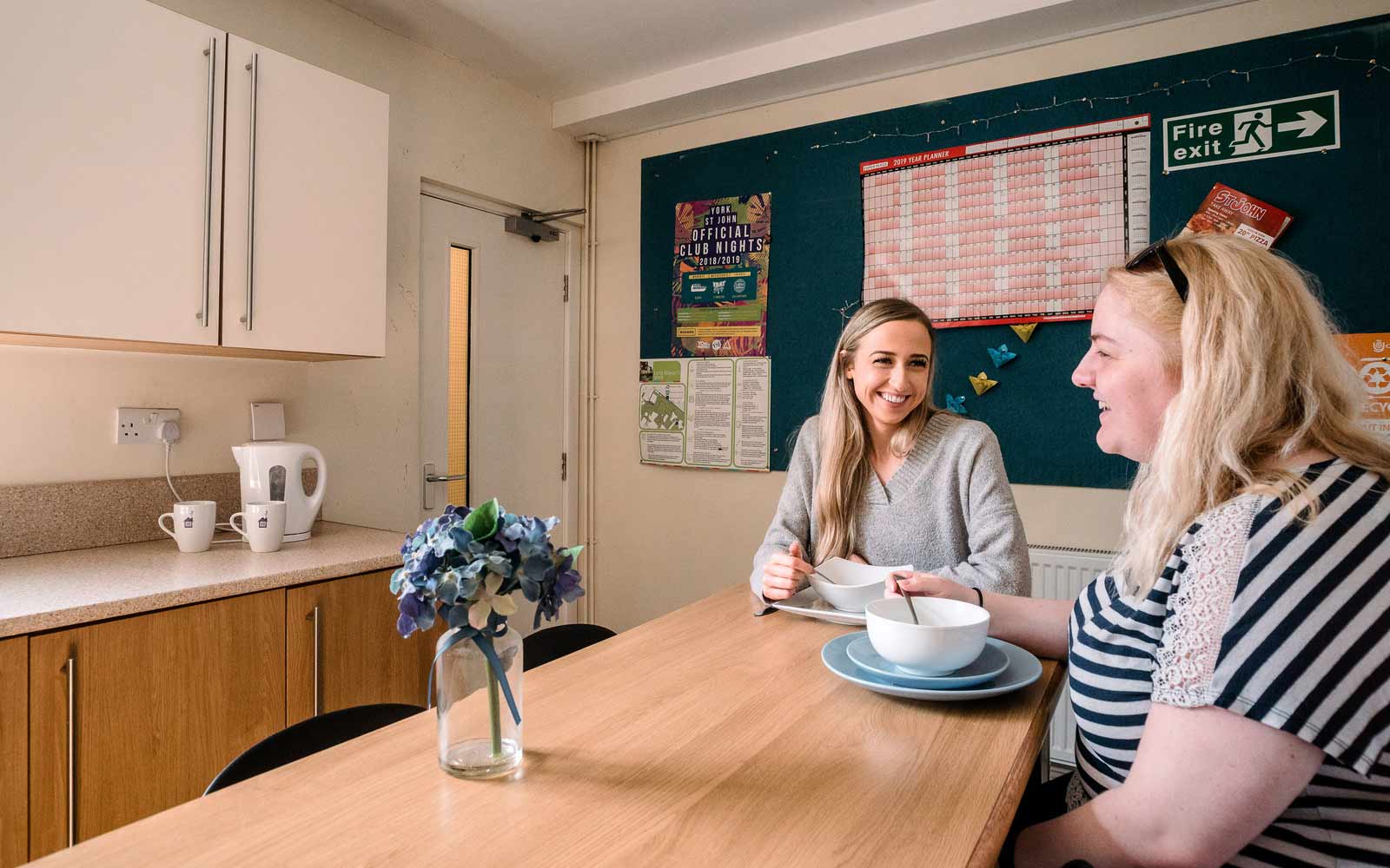 Two students chat in a student accommodation site kitchen.