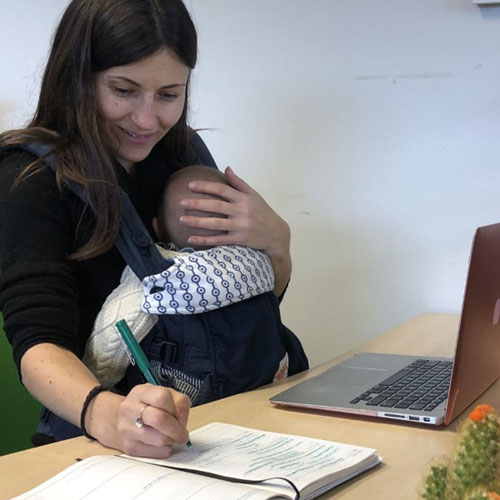 Woman holding baby and working at laptop on desk
