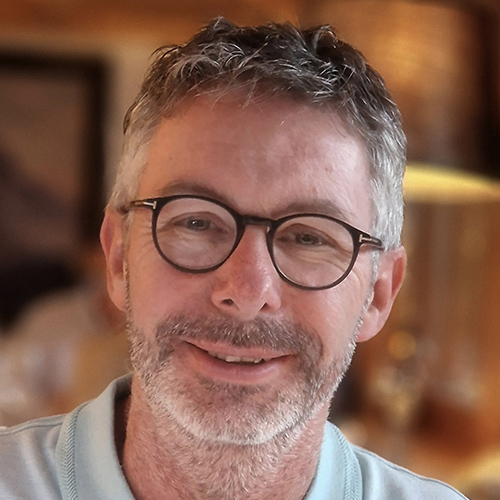 Grey haired man wearing glasses smiling at the camera