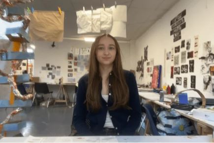 Lucy Coultert standing in an art workshop with paintings on the wall.