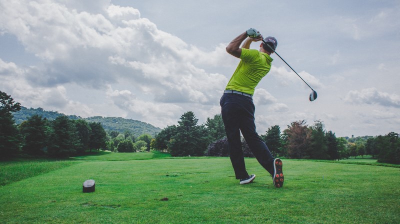 A man in a yellow top and dark trousers playing golf