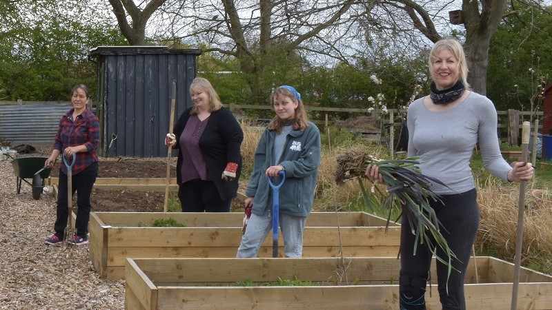 People outside at allotment garden holding produce