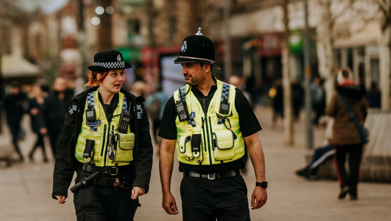 Two uniformed police officers walking on a busy high street