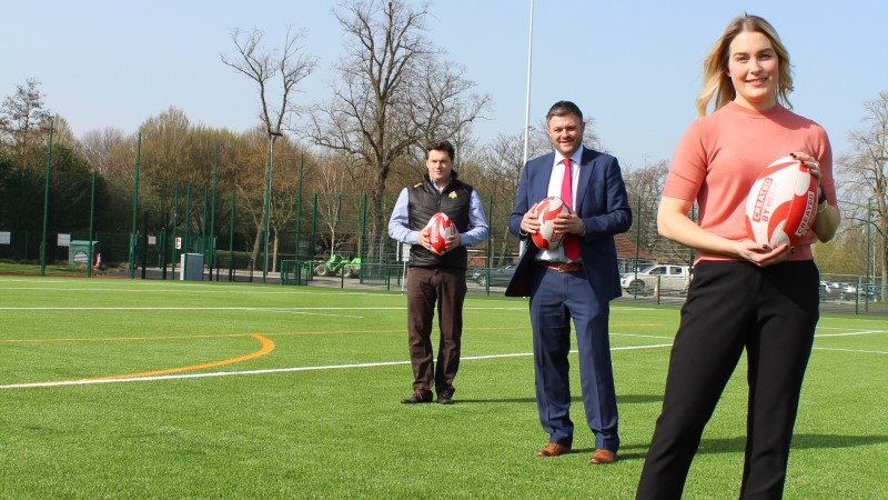 Three people in line holding rugby ball outside