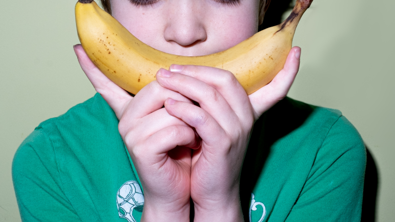 Close up of young boy holding a banana in front of his smile