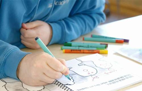 Close-up of hand holding a marker pen drawing in book.