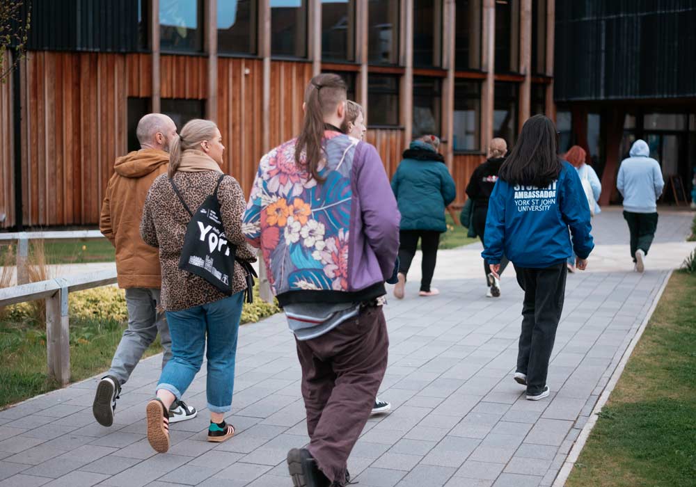 A group of visitors walking toward the Creative Centre during a campus tour at York St John University's York Campus.