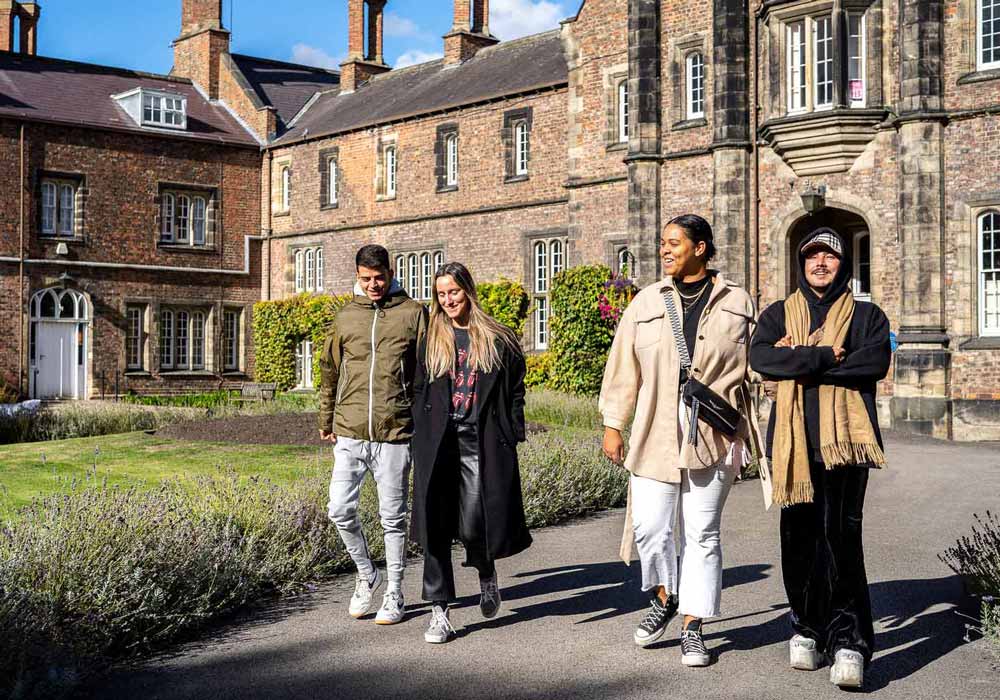 A group of students walking together in front of the sunny Quad building on York St John University York Campus.