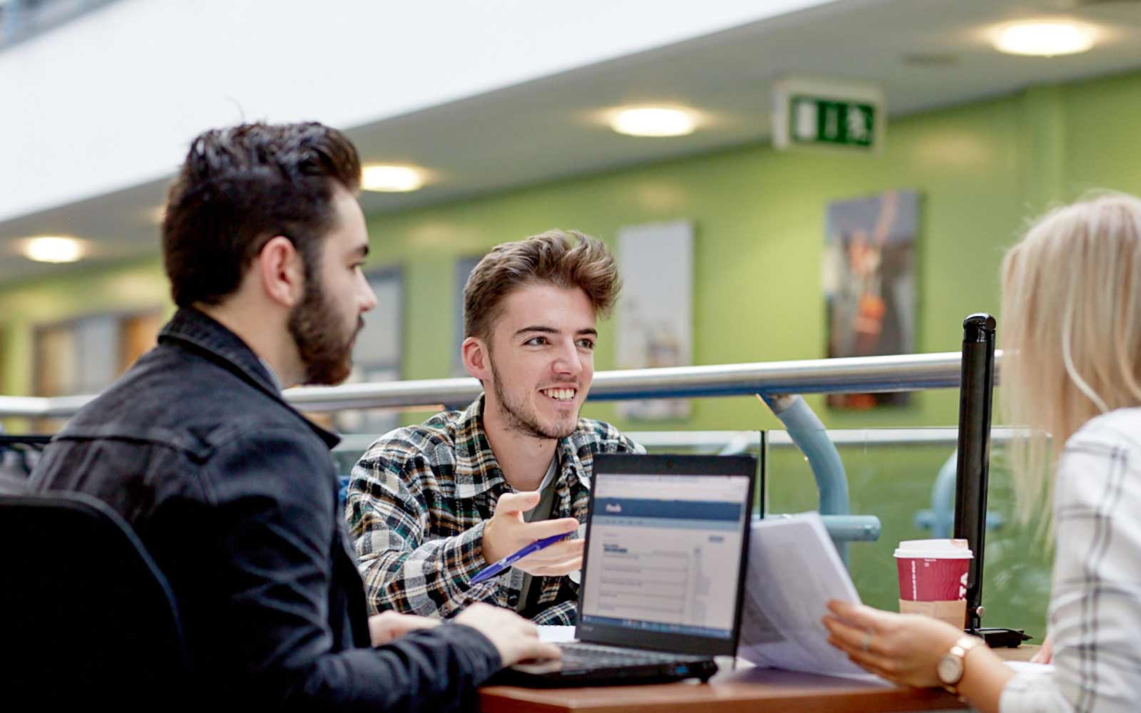 Three students study together with laptops and papers on Fountains Second Floor