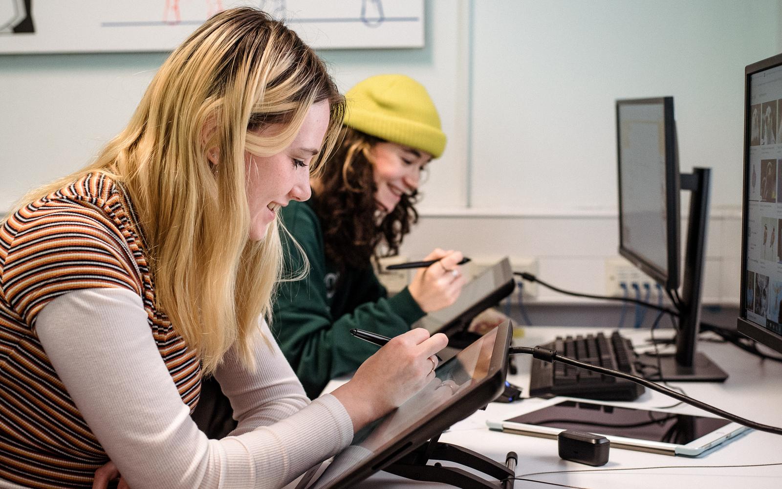 Two animation students work side by side sketching on tablets