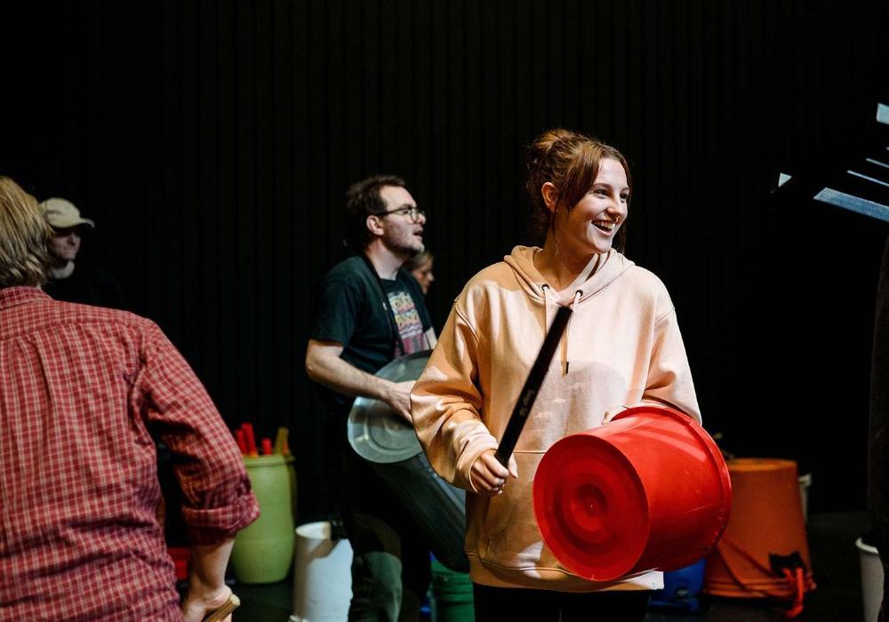 Community musicians drumming on stage with steel bins and plastic buckets