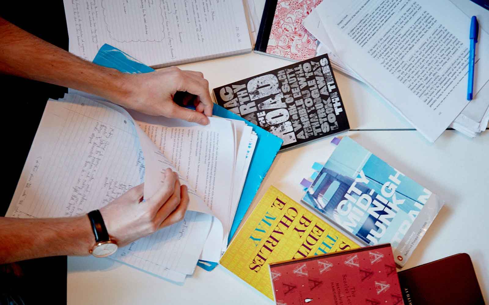 Table of study materials with hands picking up paper