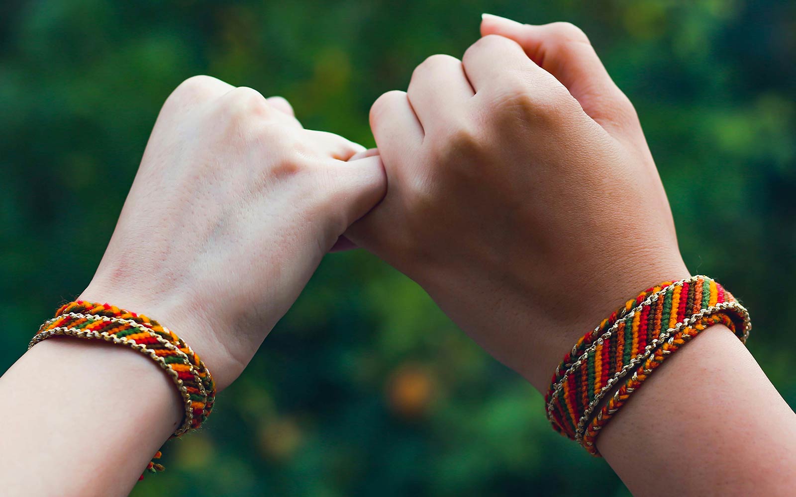 Two hands wearing friendship bracelets, little fingers entwined