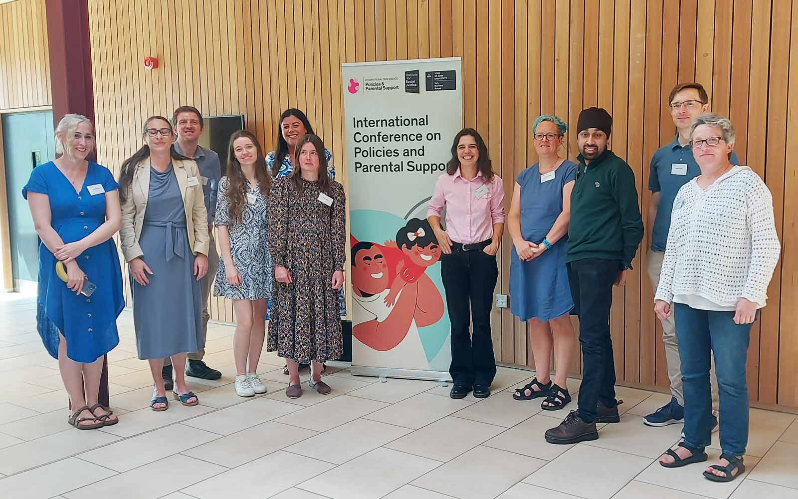Attendees of the 2023 International Conference on Policies and Parental Support standing in front of the conference banner