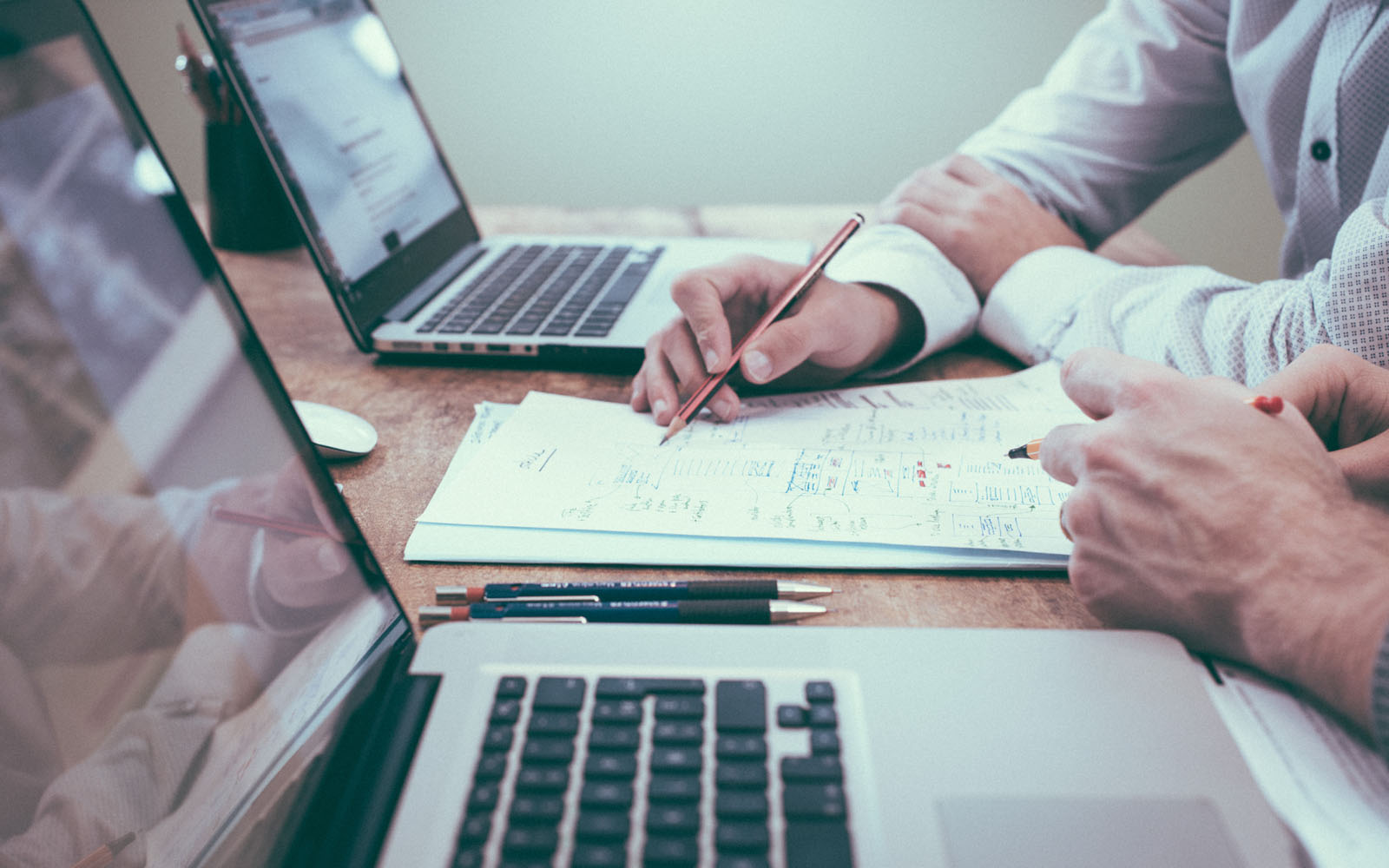 Two people sat at desk with laptops discussing ideas on paper