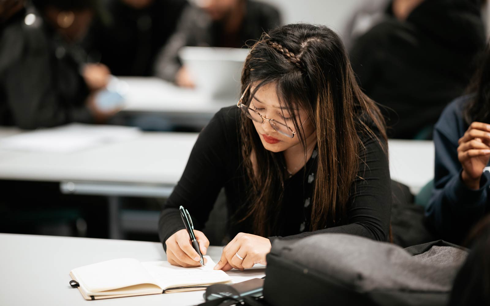 A student sat at desk making notes in a notebook.