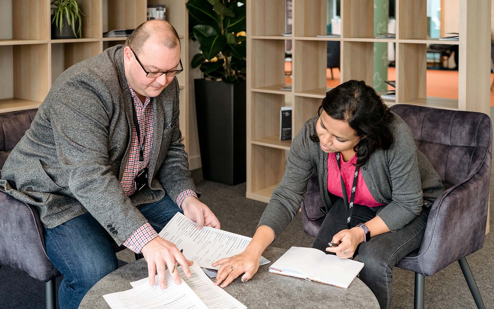 Two people sat by a table covered in paperwork at the London campus