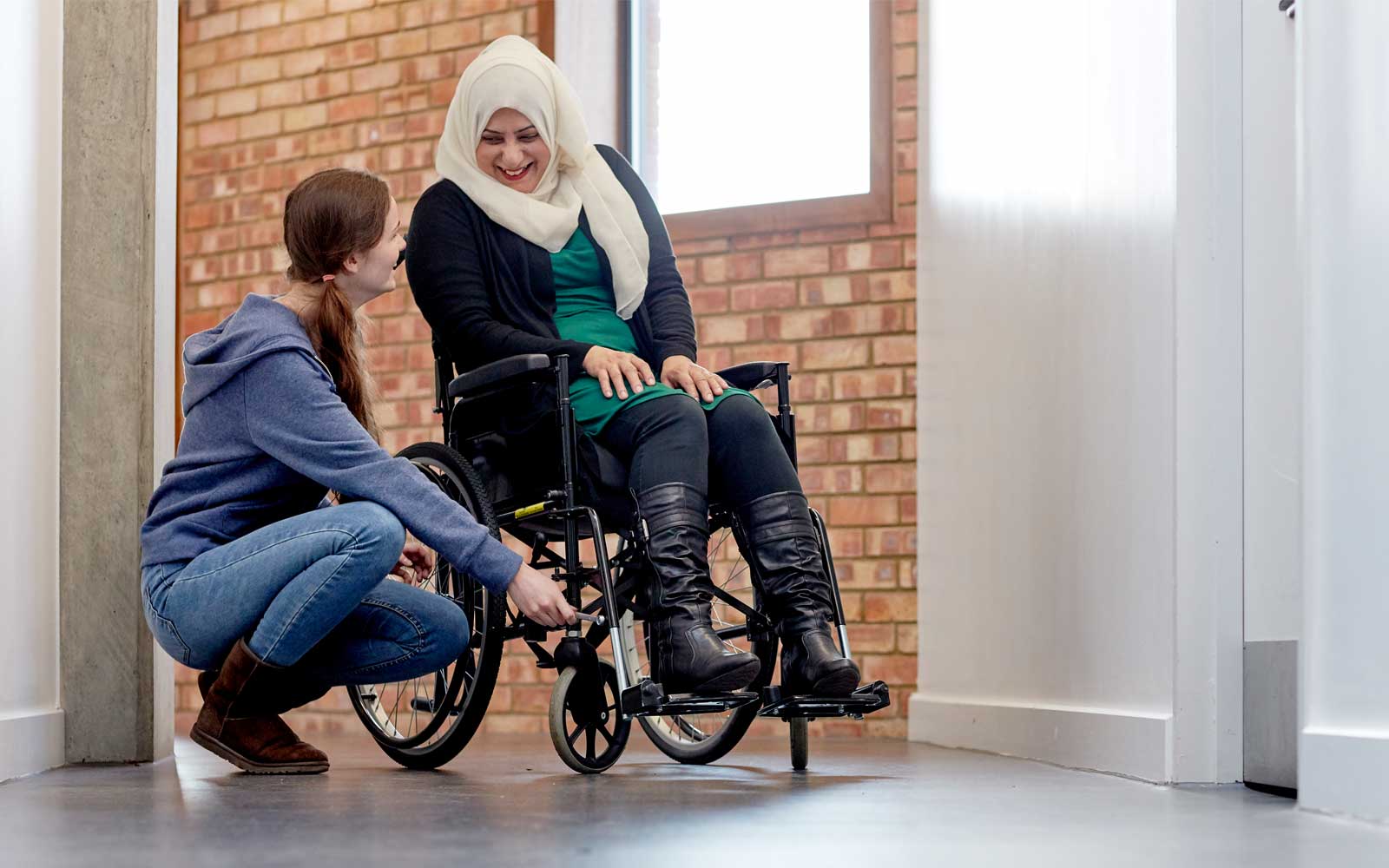 An occupational therapy student offers assistance to a wheelchair user. They are both smiling.