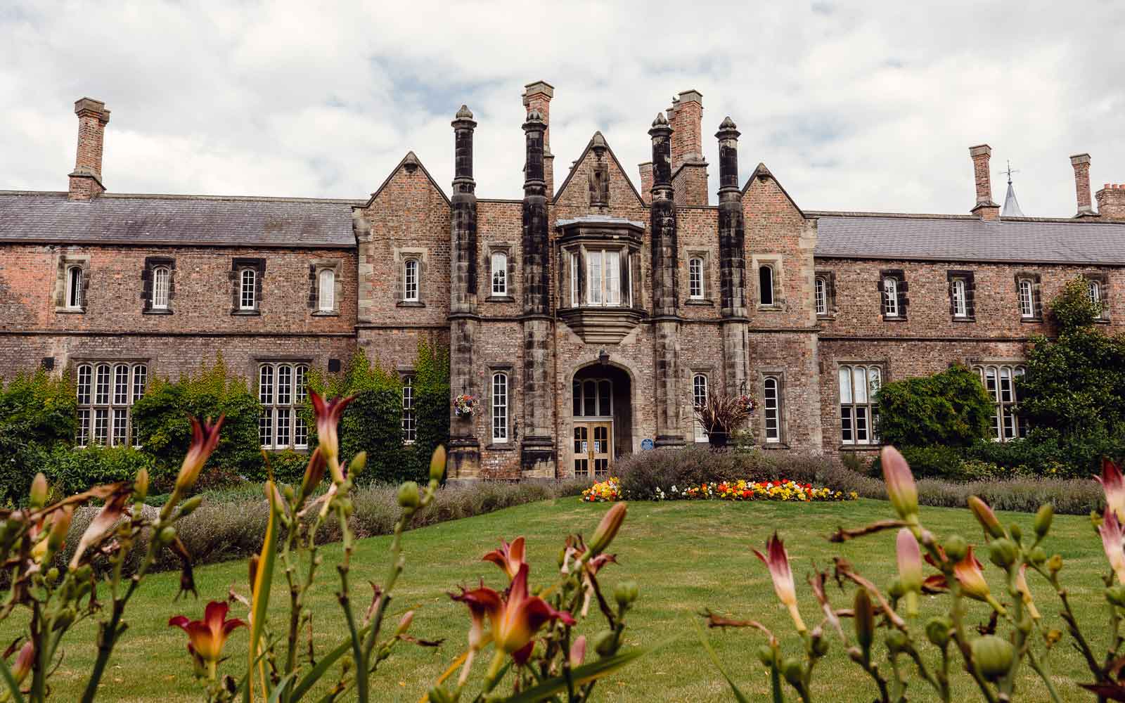 The Victorian architecture of the Quad building on our campus is pictured through orange and red flowers.