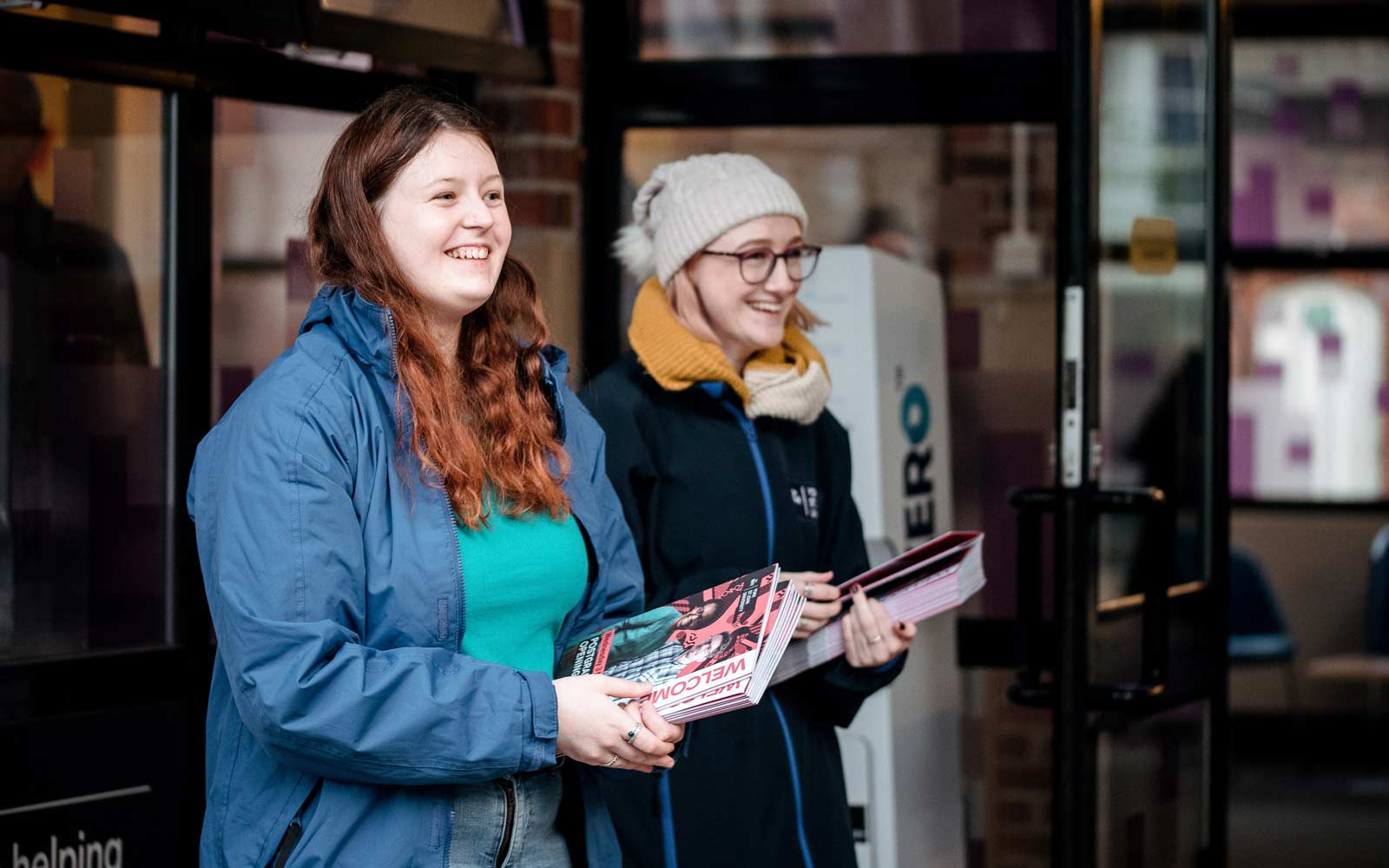 Students outside door with piles of programmes at open evening event