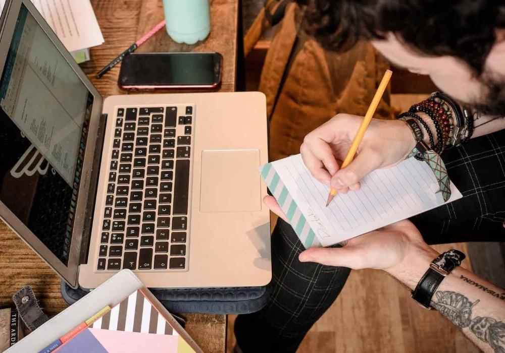 Student making study notes in front of laptop