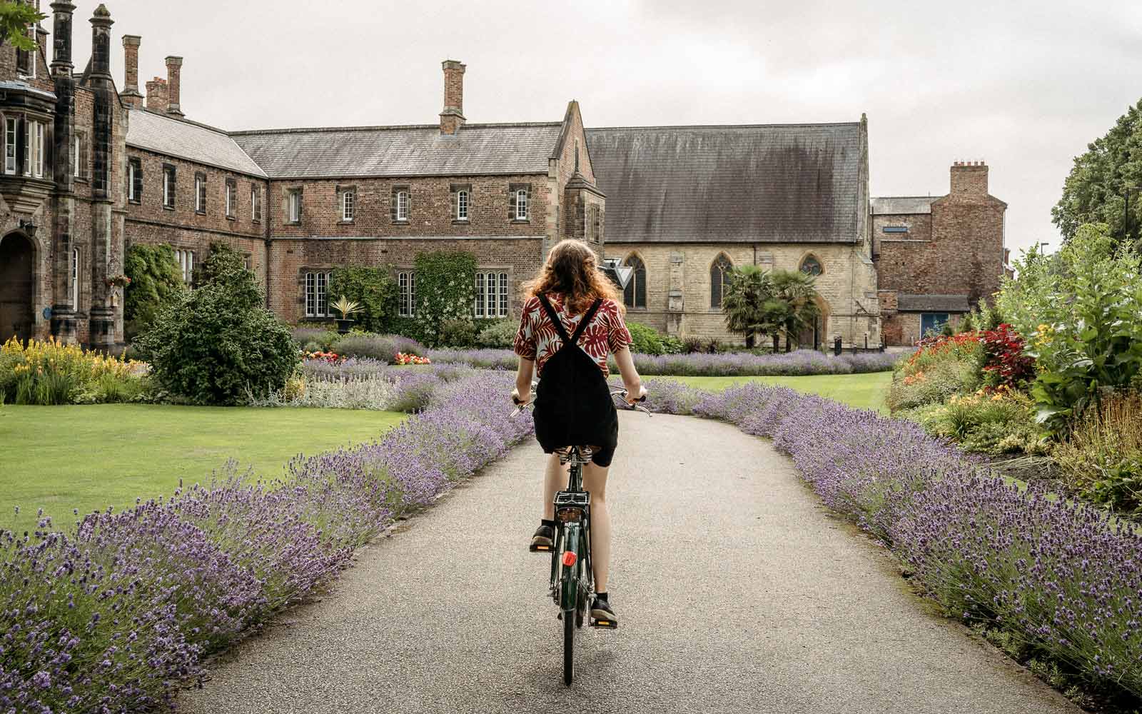 Student riding bike down path in front of campus building