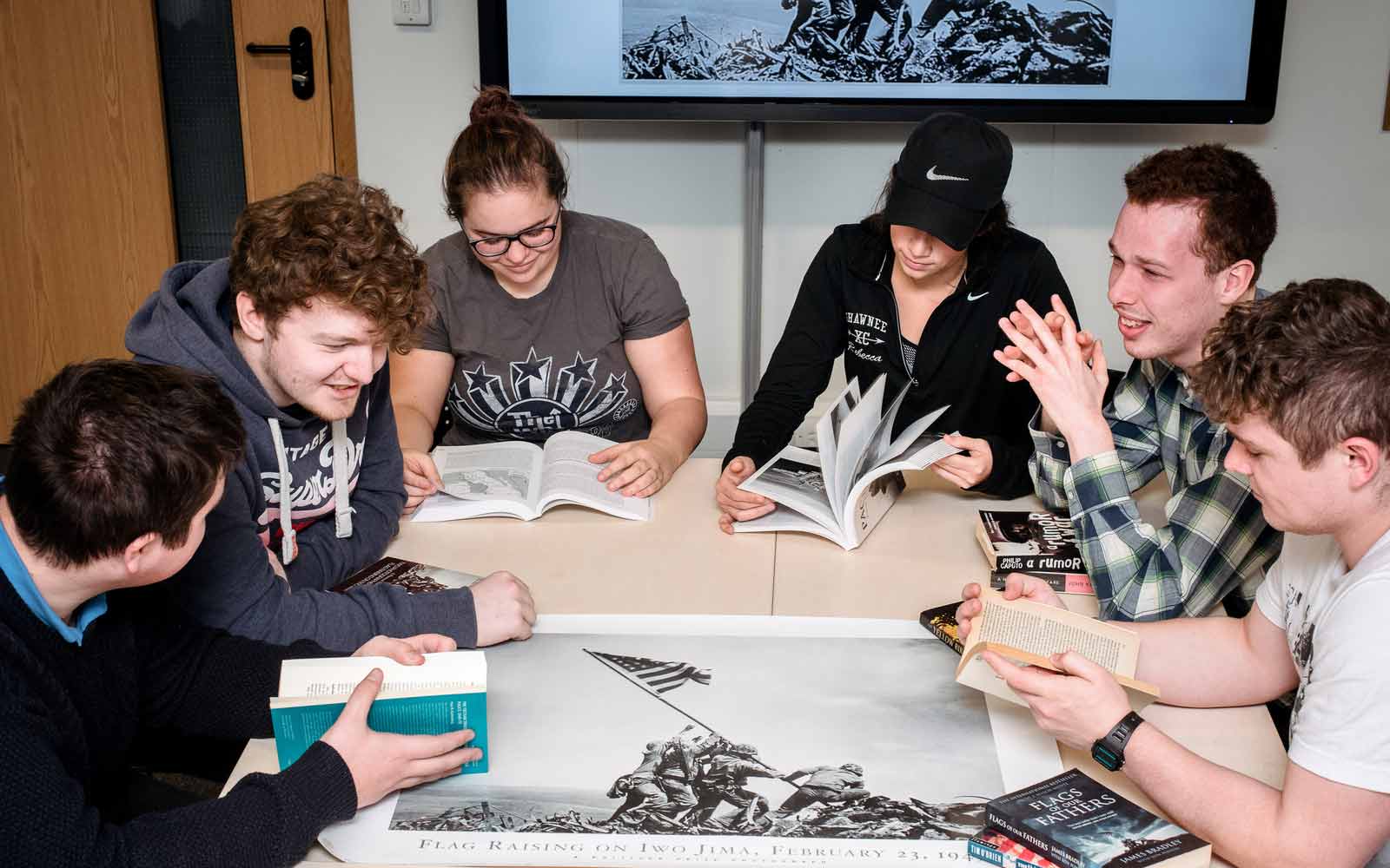 6 students sit around a table reading war studies books.