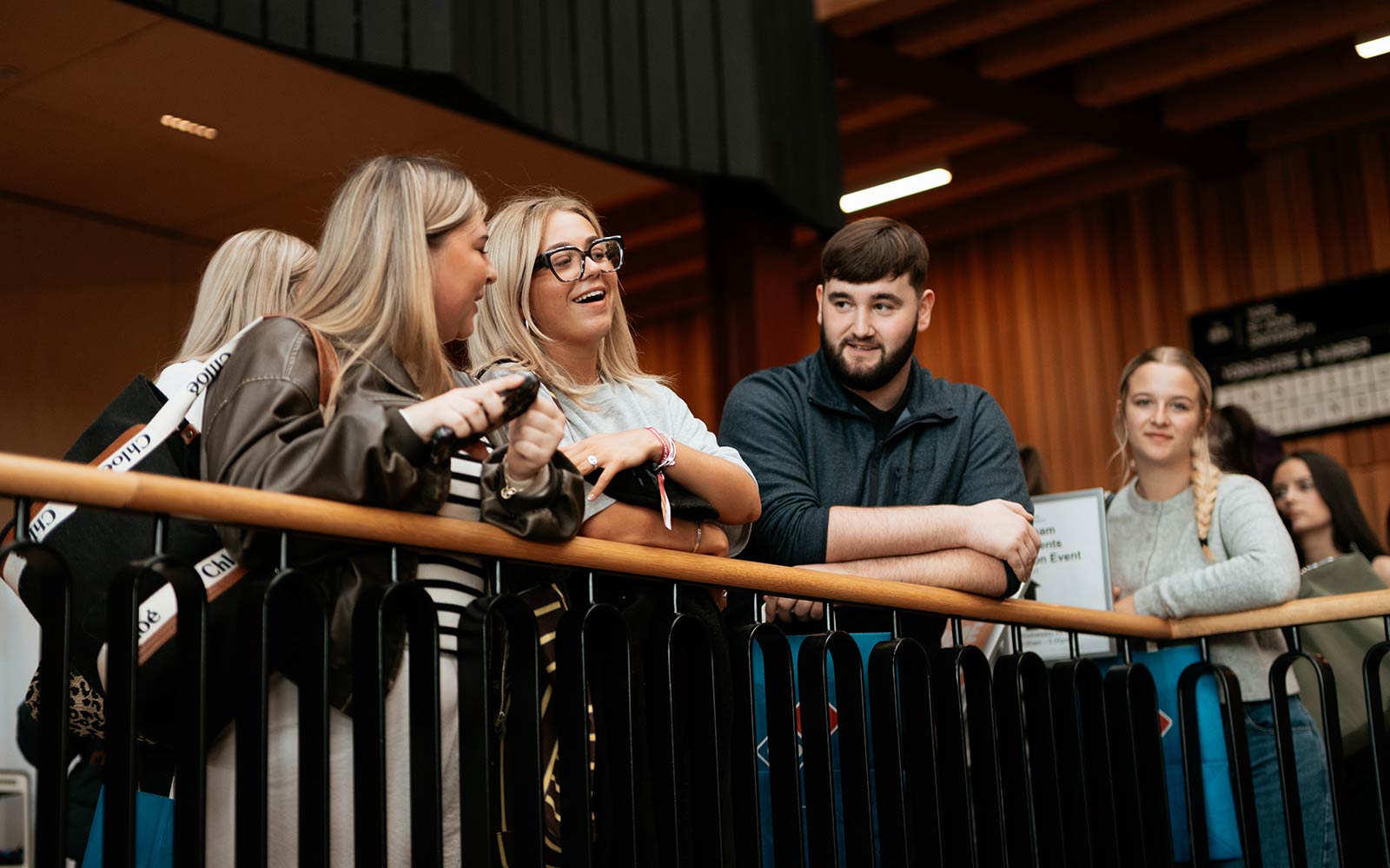 A group of students lean on the Creative Centre balcony, chatting and smiling.