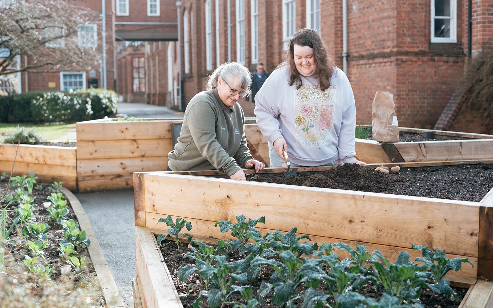 Student working with member of gardening team to add plants to raised beds