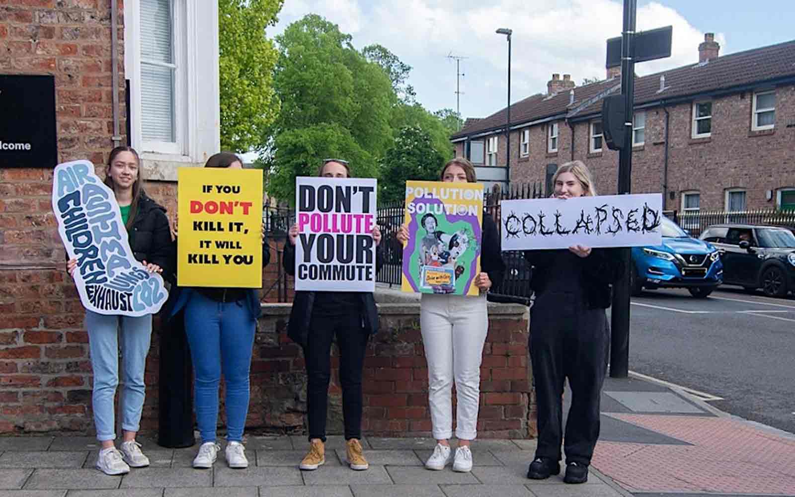 A group of students outside the De Grey building with signs.
