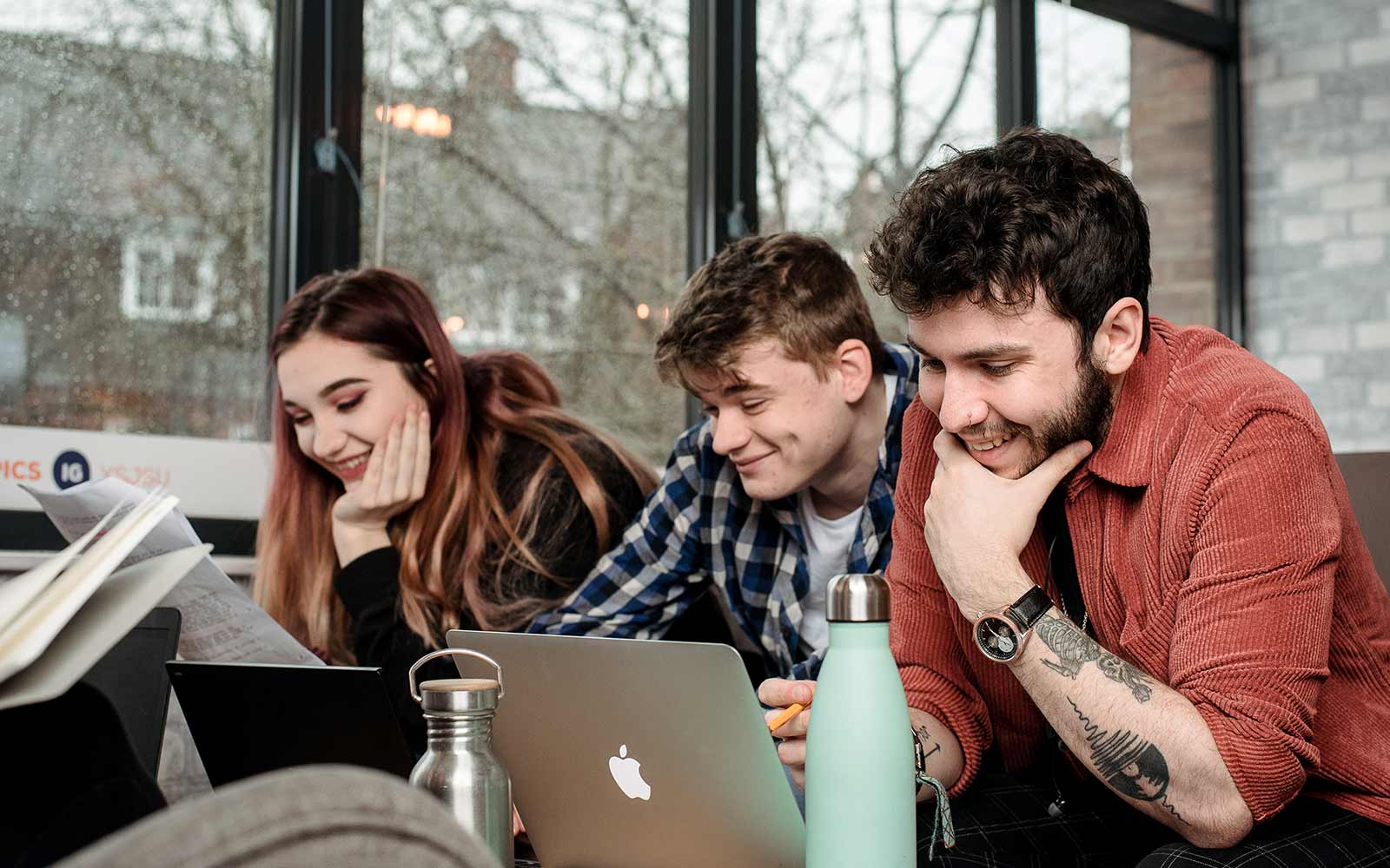three students smiling and using laptops in the SU 
