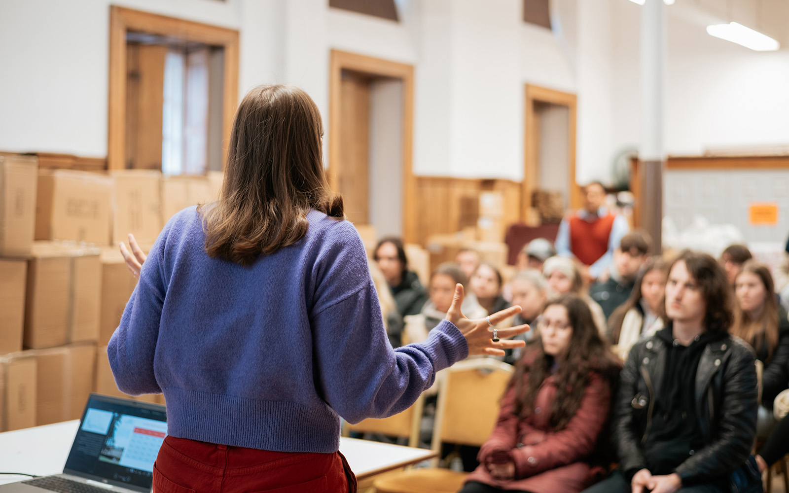 A photo is taken over the shoulder of someone giving a talk to an assembled group of people.
