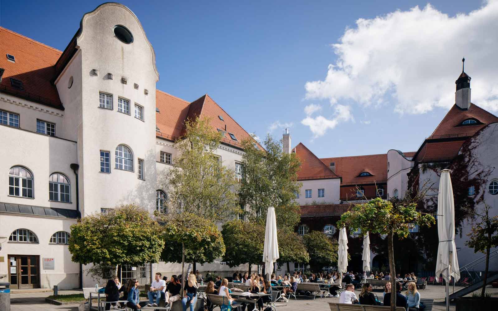 Historic square with old buildings, trees, and seating areas in Munich.