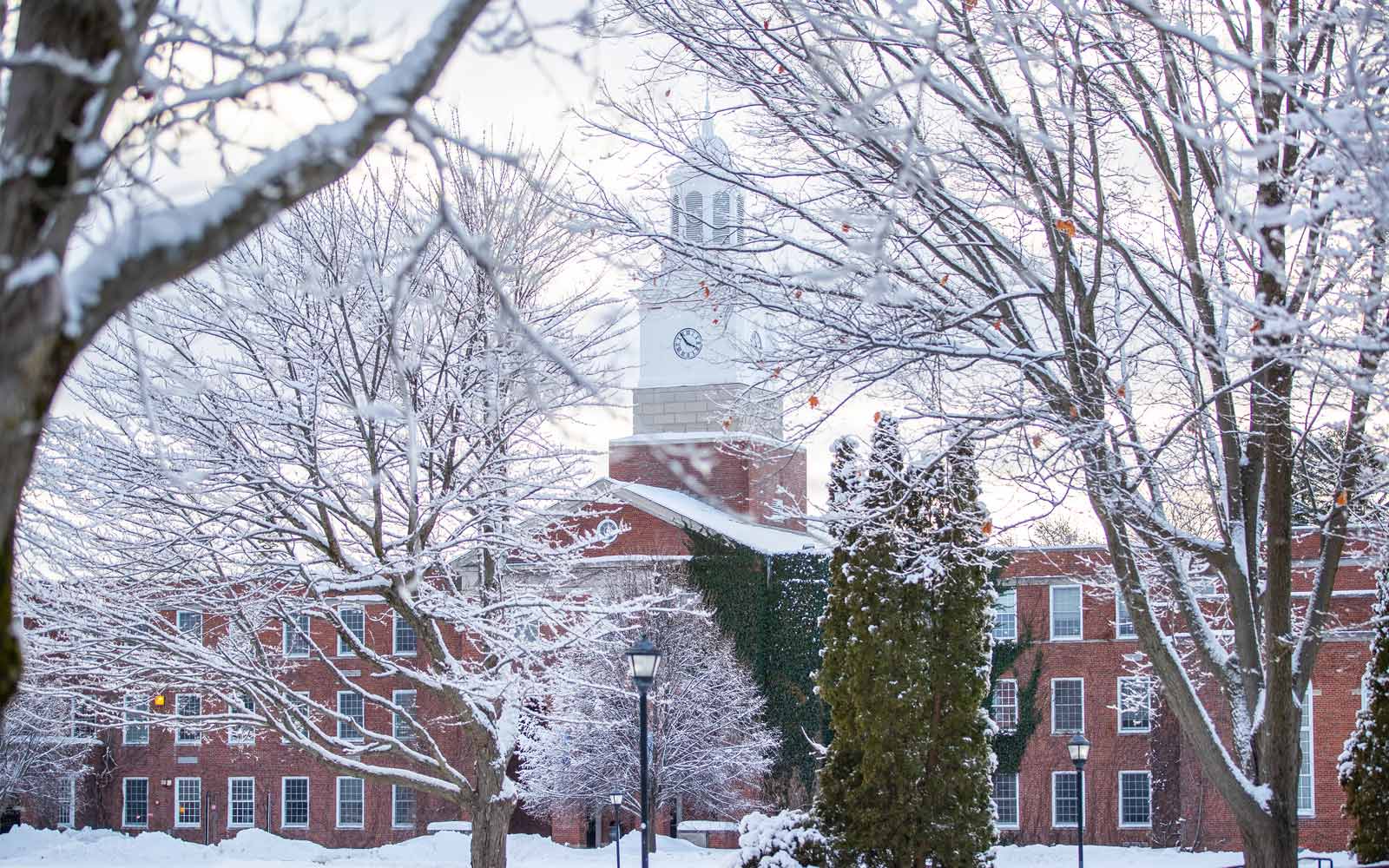 Historic clocktower building with snowy trees in the foreground, on SUNY Potsdam campus.