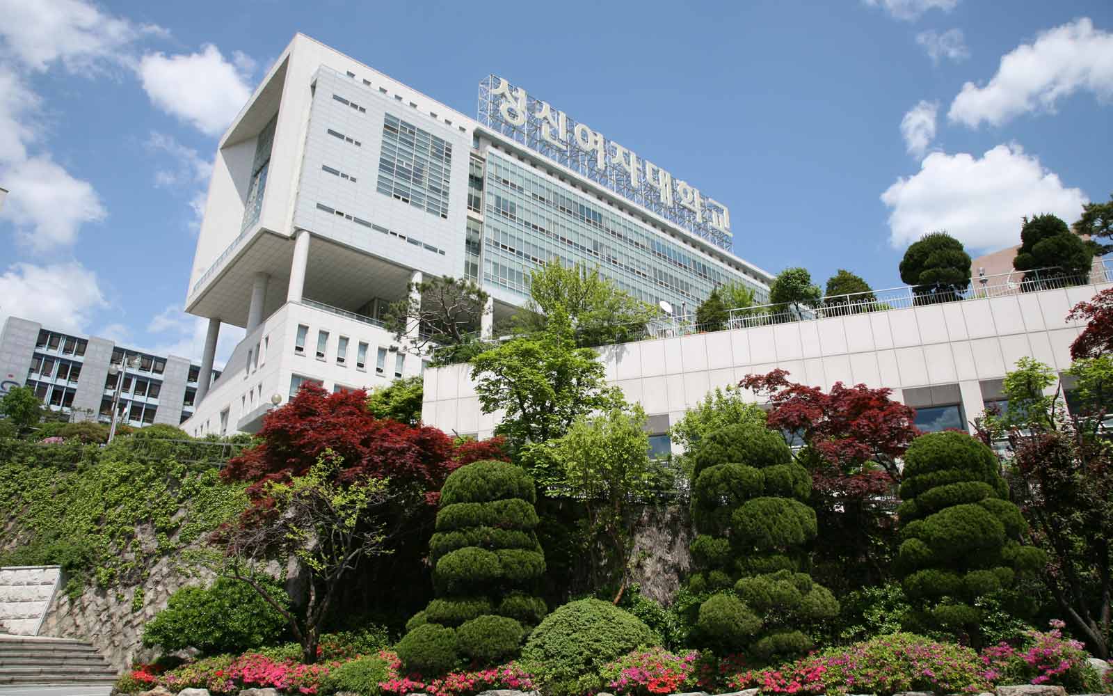 Modern campus building with Sungshin Women's University sign, with foliage in the foreground.