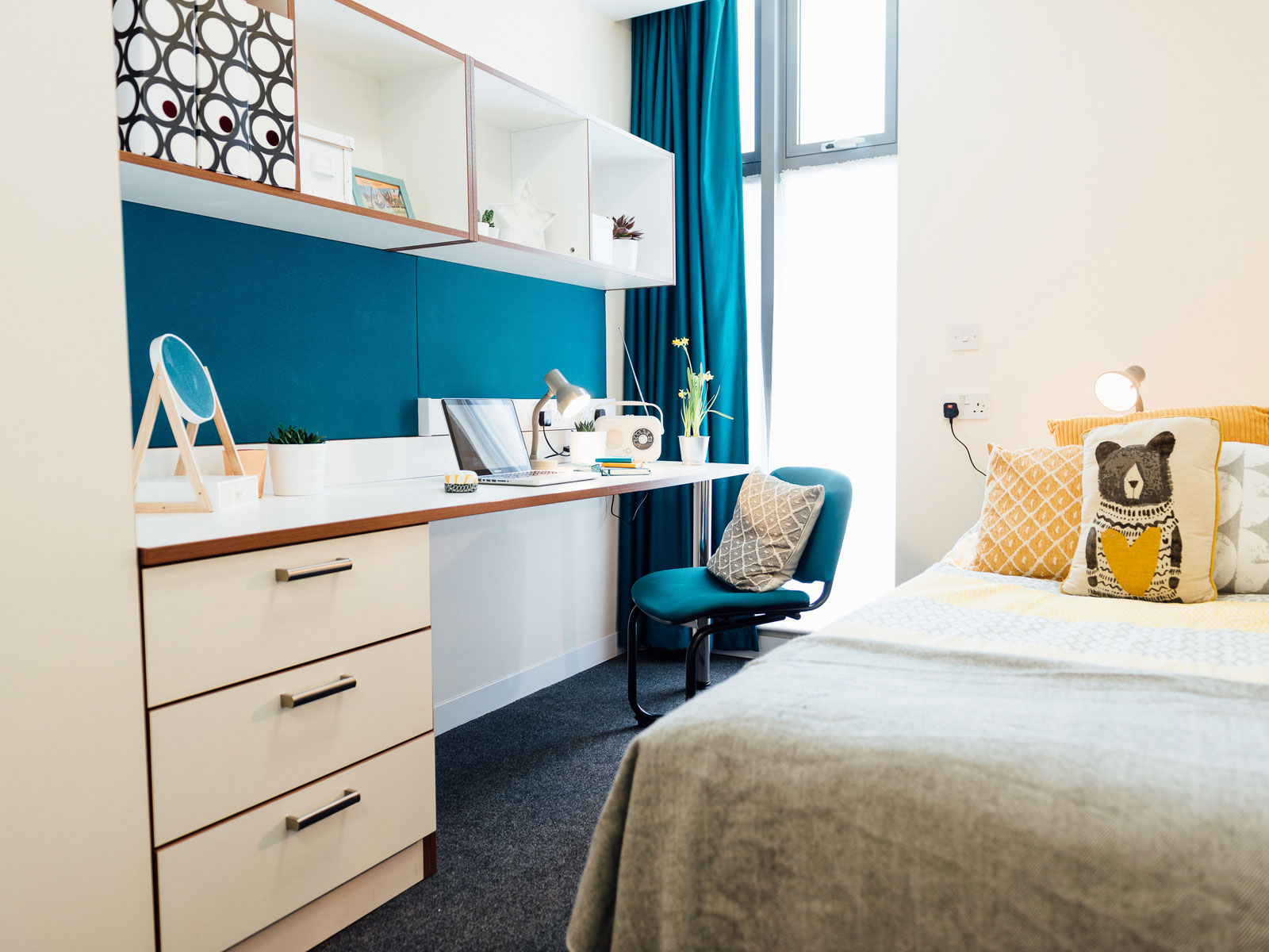 View of a single bed, desk and built-in shelving in a standard room at St John Central accommodation site.