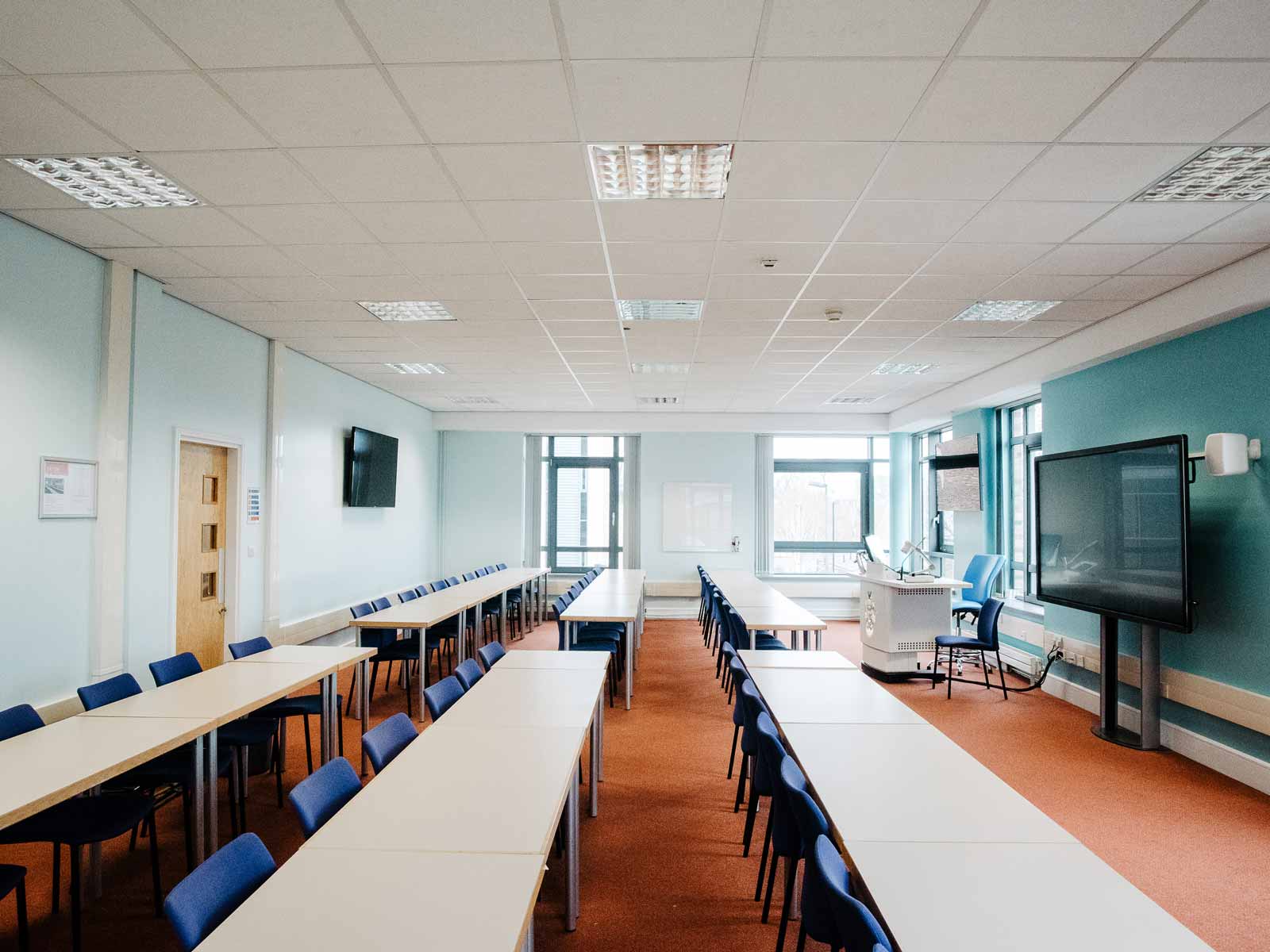 Classroom with rows of tables and chairs and a smart screen.