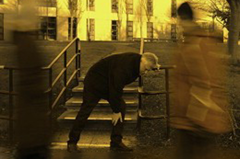 Person bent over holding leg while blurred figures walk by.