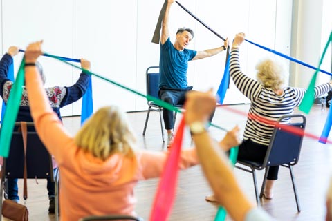 Older adults sat on chairs holding exercise bands, taking part in exercise class.