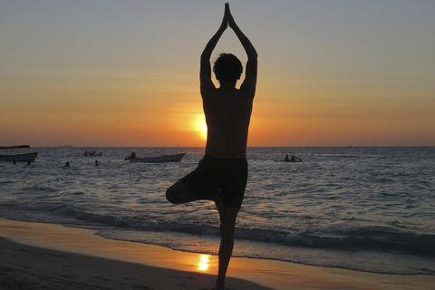 Silhouette of an individual in a yoga pose on a beach in the evening