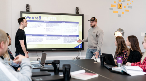 two students presenting using a white board to give a presentation to other students