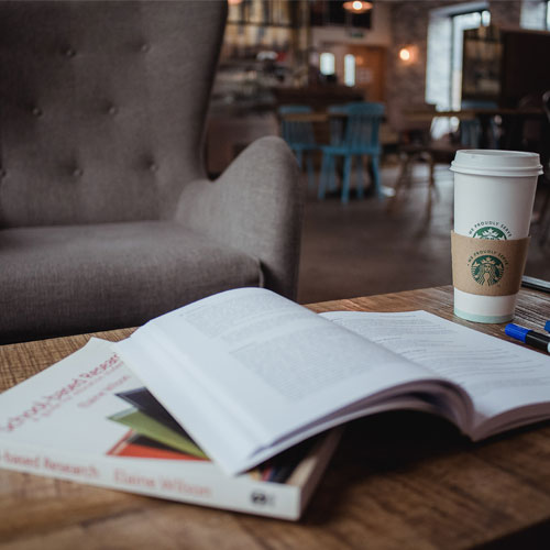 A pile of books and a coffee cup on a table. 