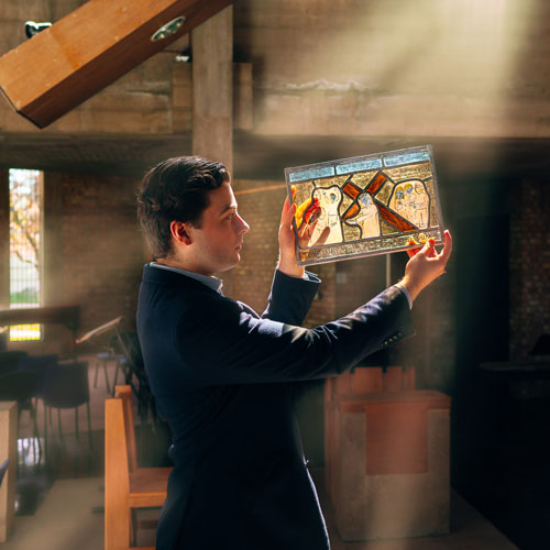 Student holding up stained glass in a sunny chapel