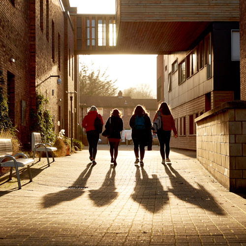 Four students walking in the sun on campus with shadows behind them