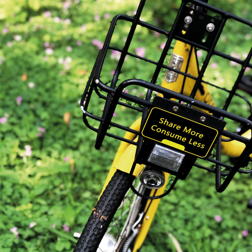 Close-up of a metal bicycle with a sign on the basket reading 'Share more, consume less'