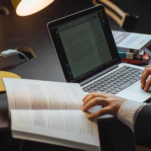 Student with textbook taking notes on laptop