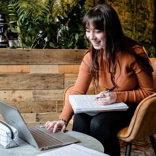 Student taking notes on laptop in cafe area