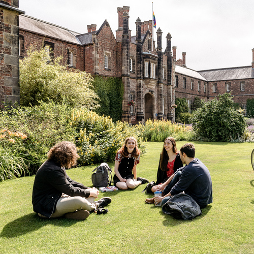 Four students sitting together on campus on the grass in front of the Quad building, on a sunny day