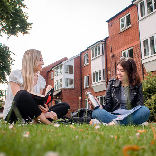 Two students chat on the grassy area outside the Grange accommodation.