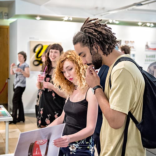 Students looking through portfolio of work at design degree show